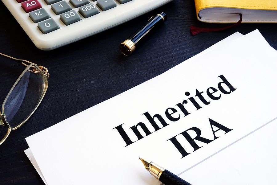 Inherited IRA paperwork on desk with calculator, glasses, and fountain pen, representing estate and retirement account planning