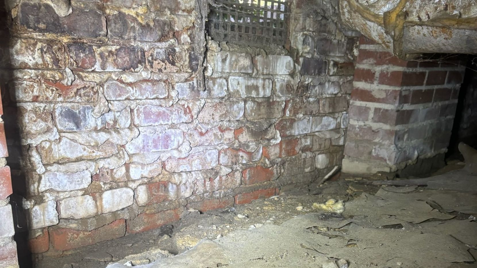 A close-up of an old brick crawl space wall showing efflorescence and signs of moisture damage.
