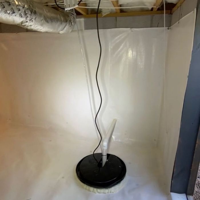 A black sump pump sits on a white vapor barrier in a clean crawl space corner, with pipes extending upwards. A black sump pump sits on a white vapor barrier in a clean crawl space corner, with pipes extending upwards.