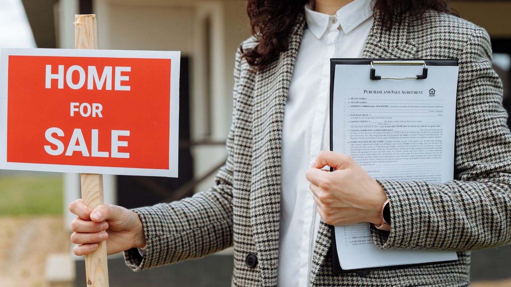 Real estate agent holding a clipboard in front of a Home For Sale sign