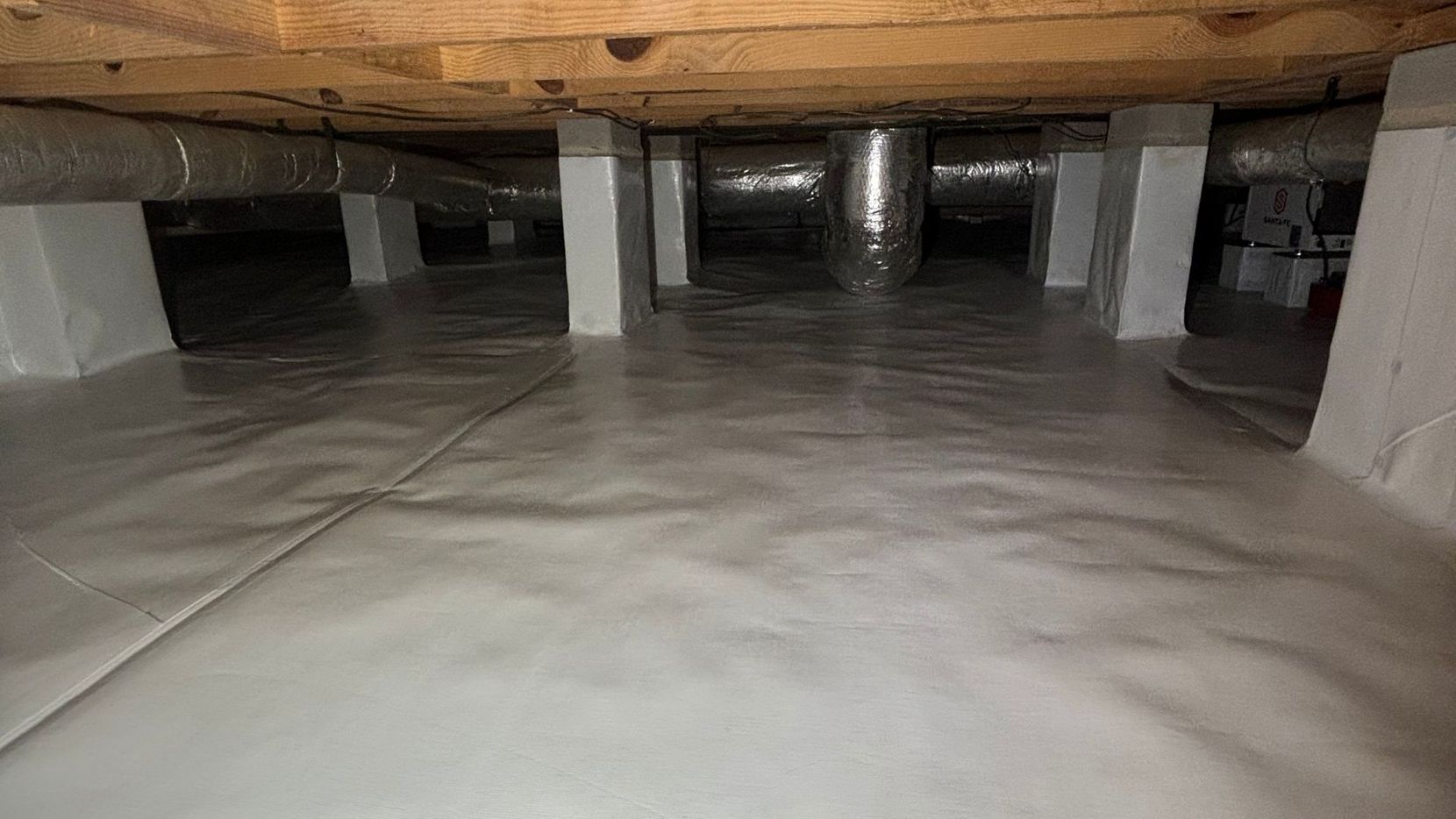 A newly encapsulated crawl space features a clean white vapor barrier covering the ground and piers. 
