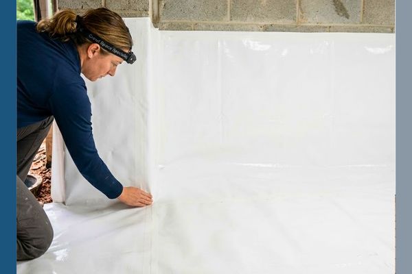 A close-up stock photo inside a dry Georgia crawl space capturing a technician from Crawl Space Specialists LLC precisely sealing a heavy-duty white vapor barrier to a concrete foundation wall during a complete encapsulation.