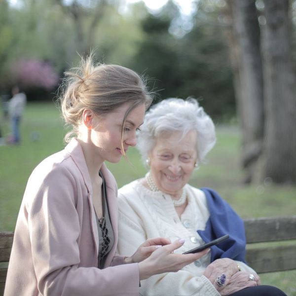 younger woman and elderly woman on park bench looking at phone