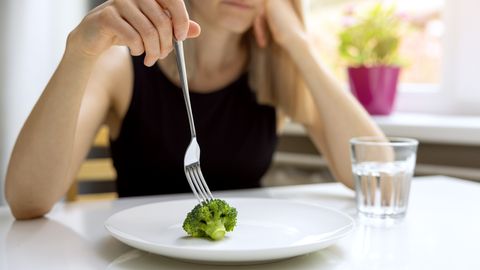 Woman reticently eating broccoli