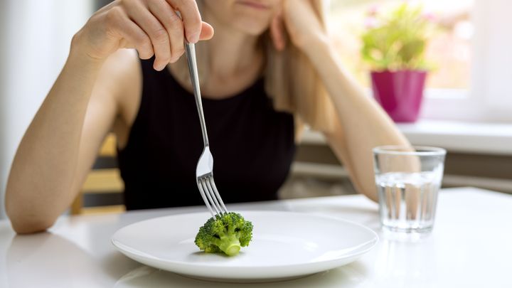 Woman reticently eating broccoli
