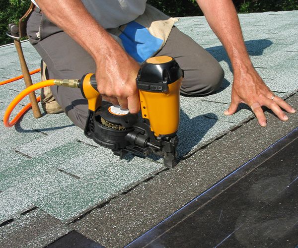 a roofer nailing roof tiles on a roof using a nail gun