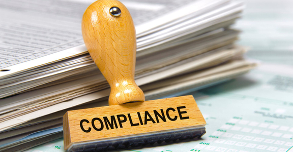 Compliance stamp leans on stack of paperwork