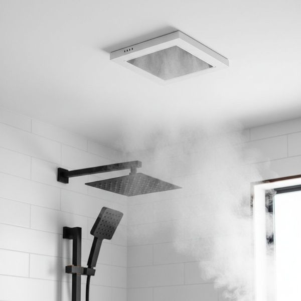 A view of a modern shower with black fixtures and white tiled walls. A square, recessed ventilation fan is mounted in the ceiling, actively pulling steam and moisture away from the shower heads.