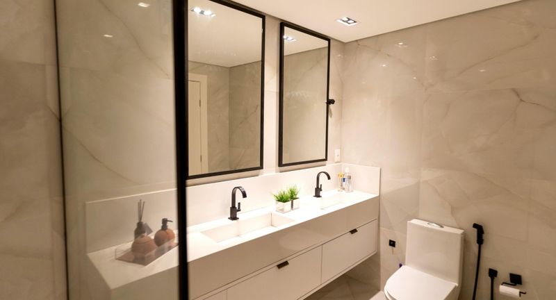 A modern, sleek bathroom with a double vanity and two large black-framed mirrors. The walls are covered in large-format marble tiles, and the fixtures are matte black. A modern, sleek bathroom with a double vanity and two large black-framed mirrors. The walls are covered in large-format marble tiles, and the fixtures are matte black.
