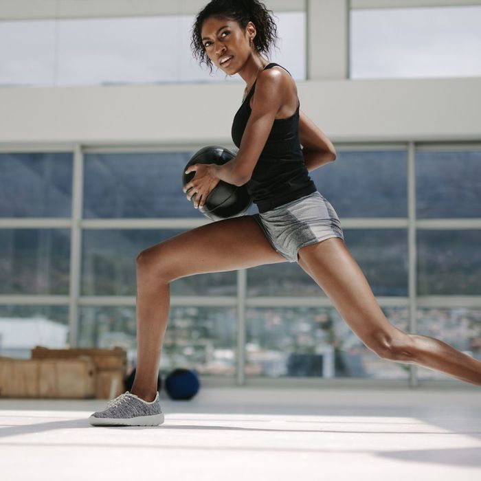 A woman doing a lunge while holding a medicine ball.