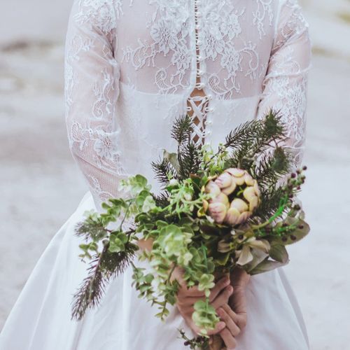a bride holding flowers behind her back with a lace overcoat