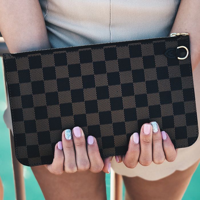 A woman holding a checkered clutch bag behind her
