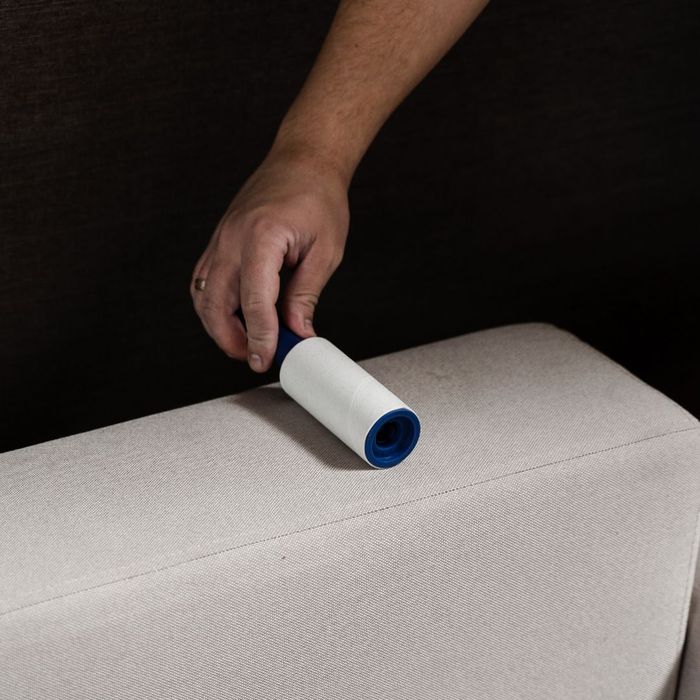 person using a lint roller on furniture