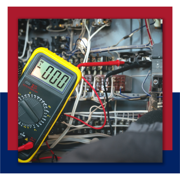 A close-up view of a yellow digital multimeter being used to test complex electrical wiring in a control panel.