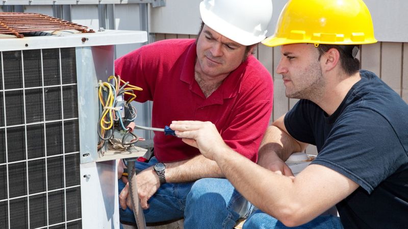 Two technicians working together to repair an outdoor AC unit. Two technicians working together to repair an outdoor AC unit.