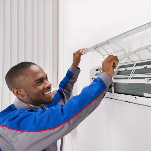 Smiling technician installing a clean air filter in a wall unit.