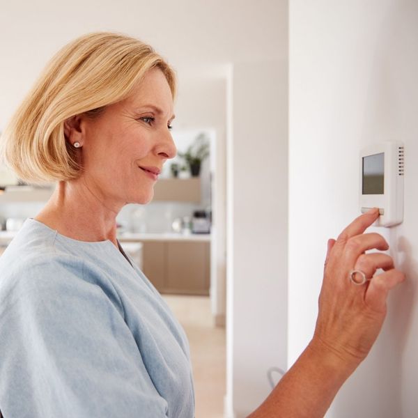 Woman adjusting a digital wall thermostat in her home.