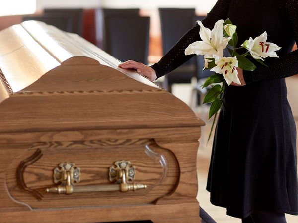 Woman holding flowers and touching a coffin.