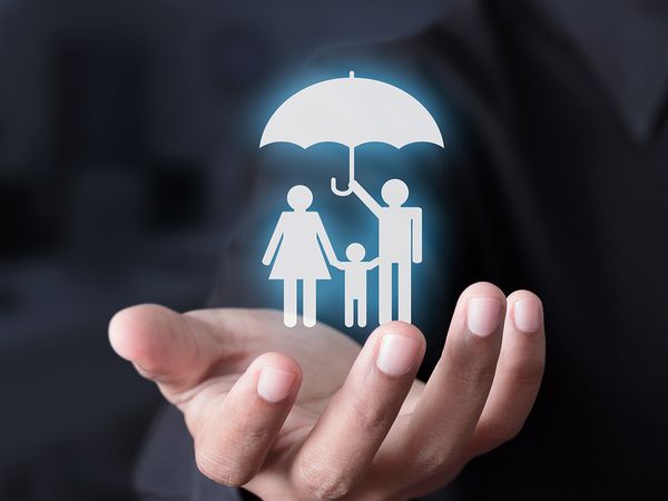  Life insurance consultant wearing a suit holds digitized family figures holding an umbrella in his hand.