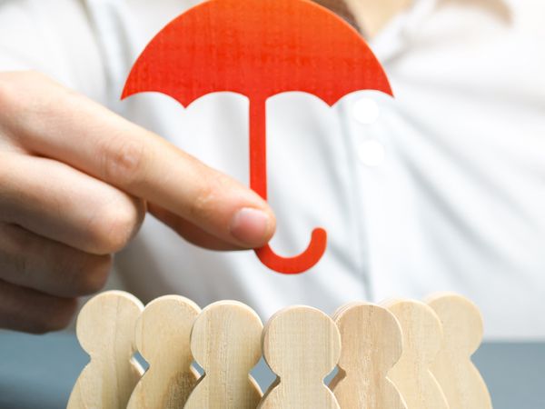 Man holding umbrella over wooden people figures.