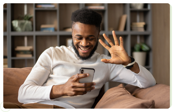 man on couch waving to phone - video call