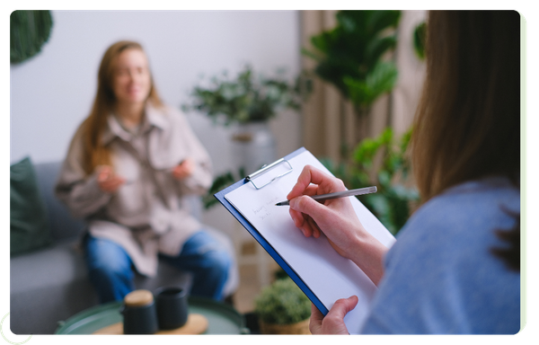 therapist writing on clipboard, client out of focus in background