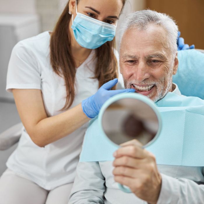 an older man smiling and looking at his new teeth with a dentist