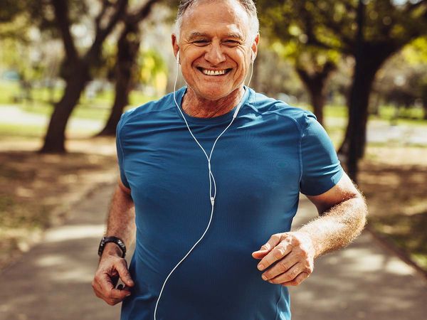 Portrait of a senior man in fitness wear running in a park. Close up of a smiling man running while listening to music using earphones