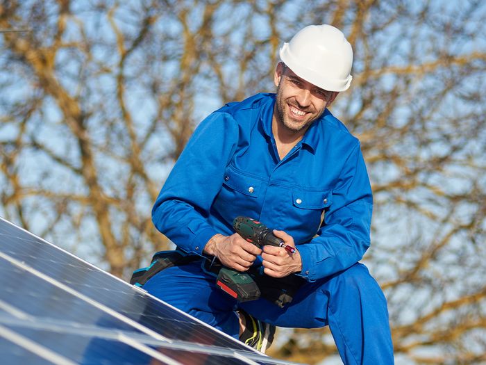 A male solar technician installing rooftop solar panels on a home.