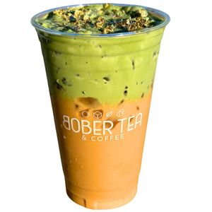 A stunning layered beverage featuring a bright orange Thai Tea base topped with a thick, vibrant green Pandan coconut cloud foam. 