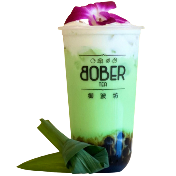 A refreshing Mung Bean Milk Tea with a soft green hue, topped with a creamy milk cap and a fresh purple orchid flower. This unique drink includes a layer of sweet boba pearls and is styled with fresh pandan leaves.