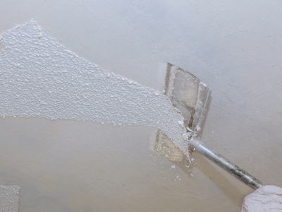 A scrapper removing popcorn ceiling material