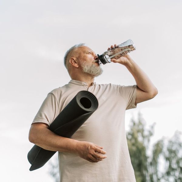 man drinking water and holding a yoga mat 