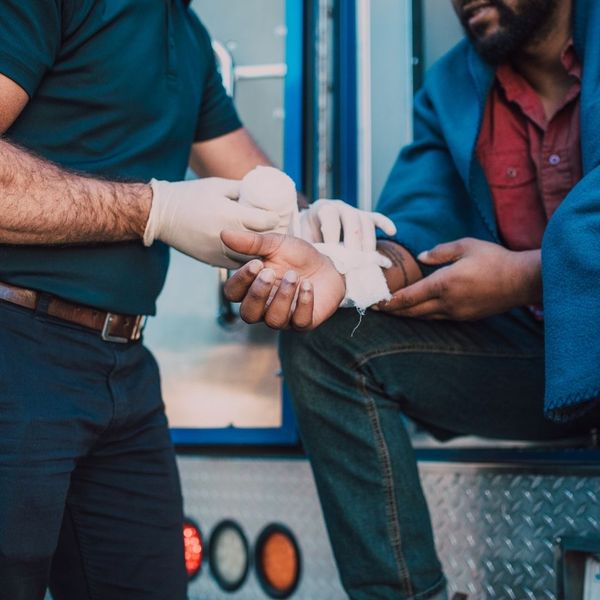 A medical professional in white gloves wraps the arm of an injured person with a bandage while standing next to an ambulance.