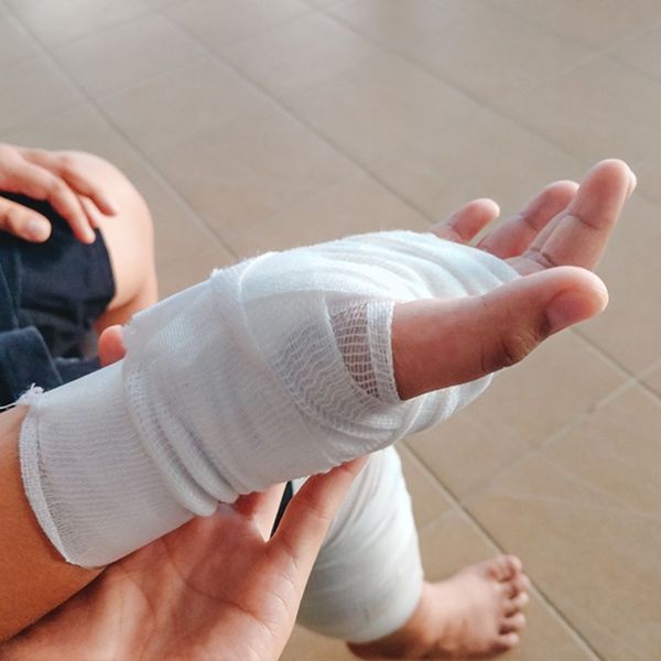 A close-up shot of an injured person's hand and wrist, wrapped in a white bandage.