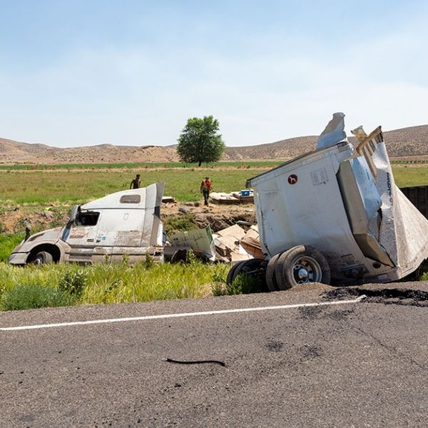 A wide shot of a highway accident involving an overturned and heavily damaged semi-truck.