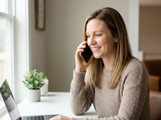 Smiling woman talking on phone and using laptop