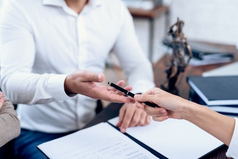 A person handing another person a pen to sign paperwork