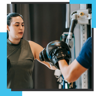 female hitting personal trainer boxing pads in gym