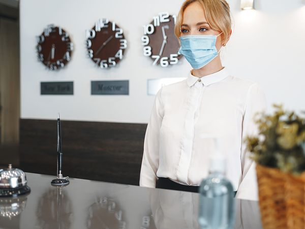 photo of woman wearing a mask behind the check in counter of a hotel