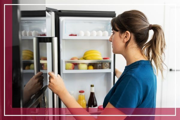 A woman with her hair in a ponytail looks inside a refrigerator that is stocked with food Old Westbury 3.jpg