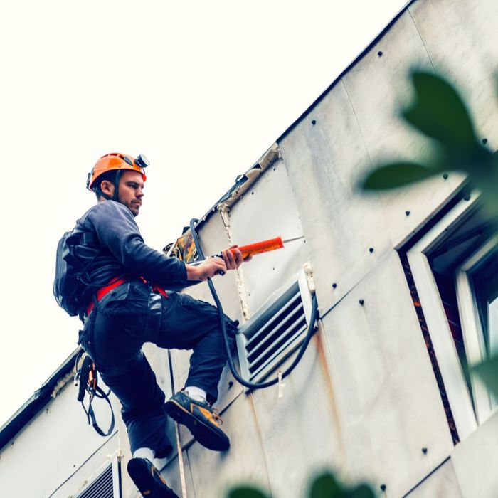 A worker hanging on the side of a building with tools
