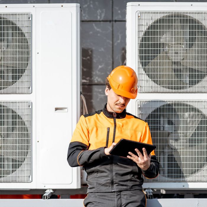 WOrker on tablet standing in front of a commercial HVAC system
