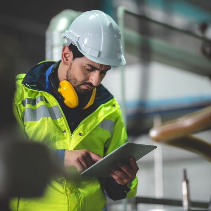 A worker in hardhat and vest reading a tablet