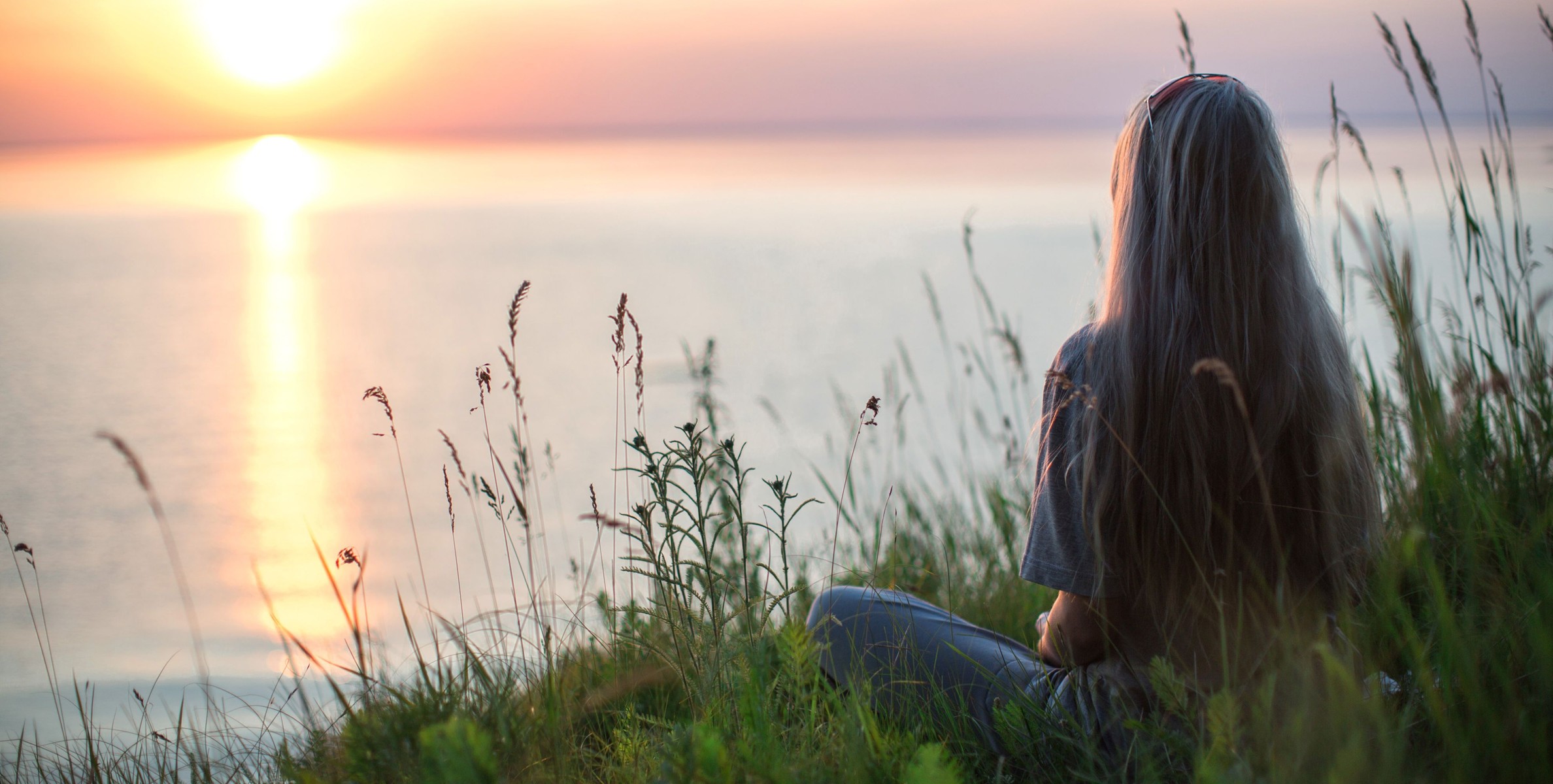 Woman sitting by the water watching the sun set