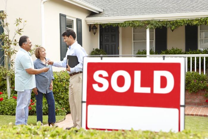 people accepting keys from a man with a sold sign outside a house