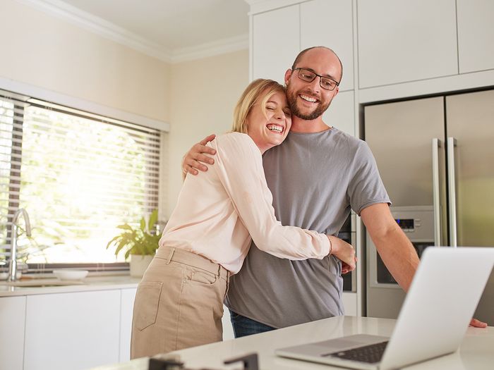 A happy couple hugging while looking at their laptop