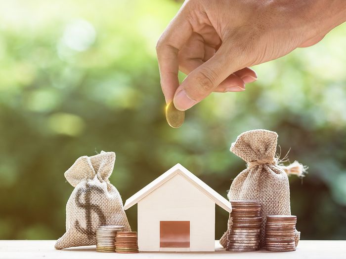 An image of a hand placing money around a little wooden house