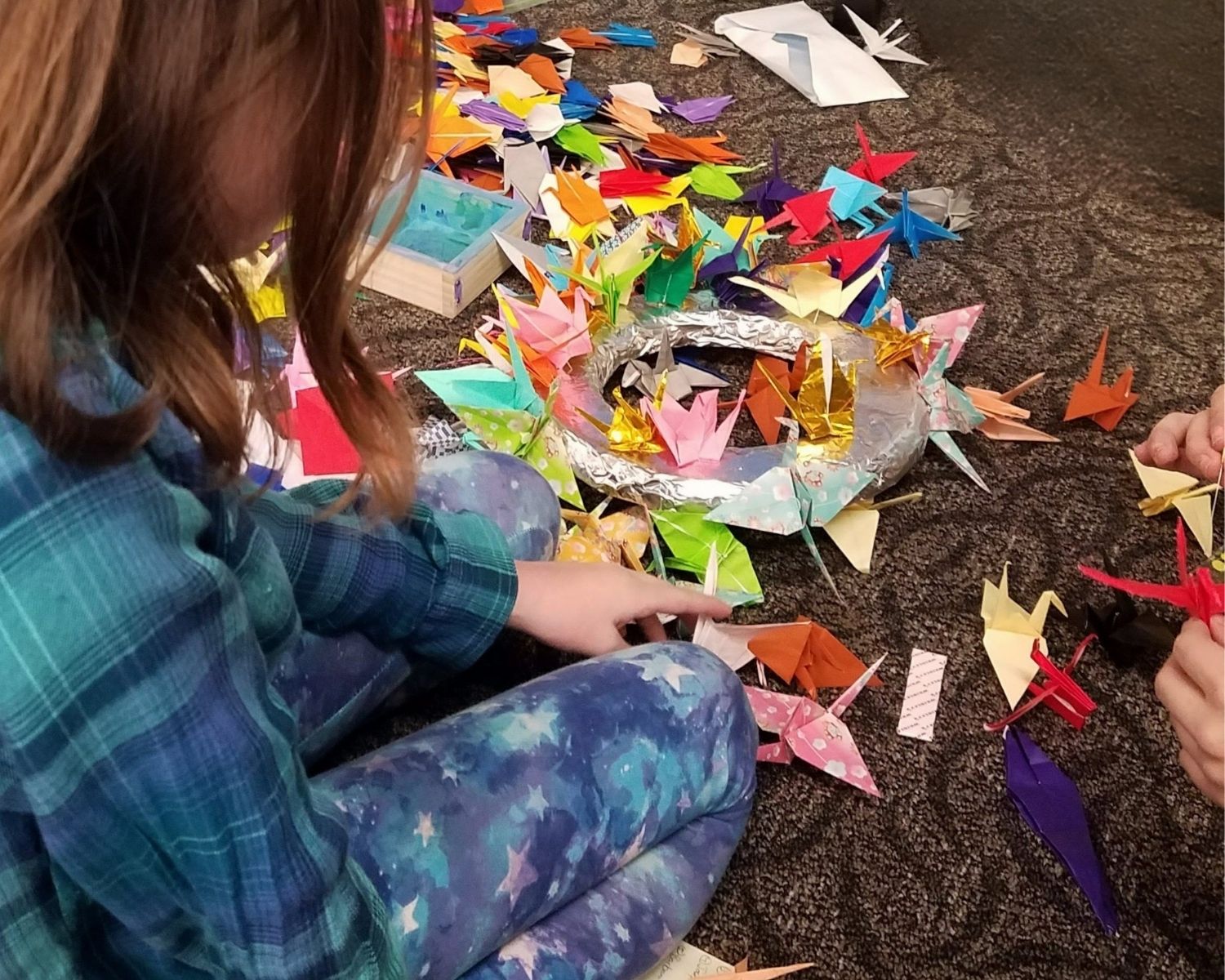 Hands making paper cranes among hundreds of finished ones