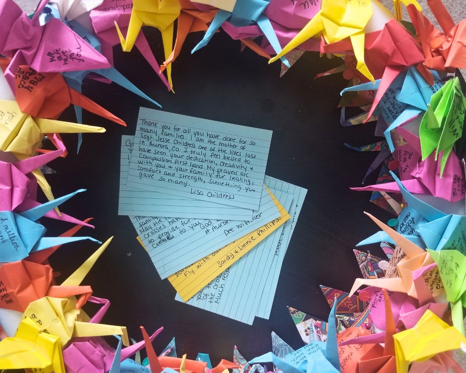 A wreath of paper cranes surrounding handwritten notes of hope